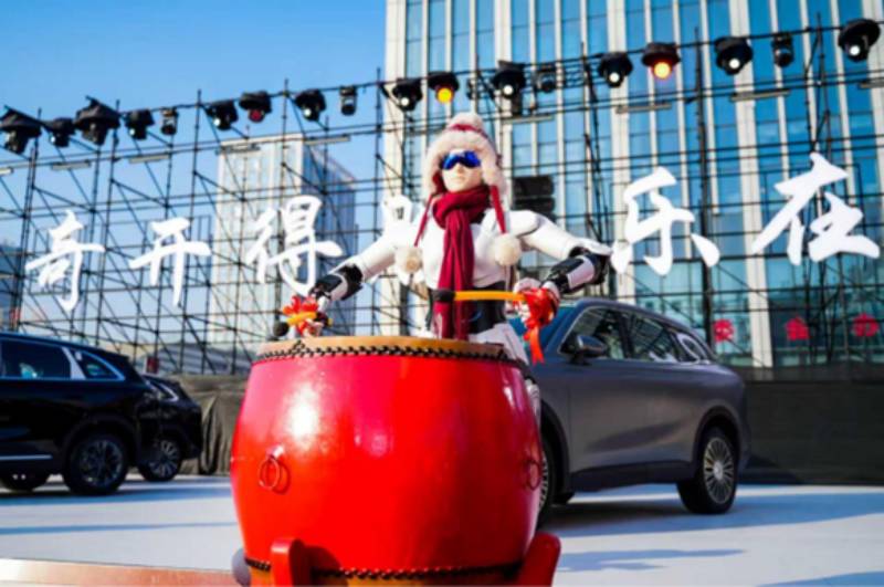 Robot humanoide de Chirey durante una demostración pública en un escenario urbano con vehículos y estructuras metálicas al fondo.